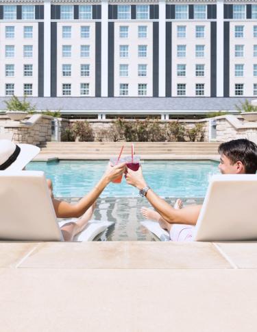 Two guests toasting glasses together while lounging poolside at the Guest House at Graceland