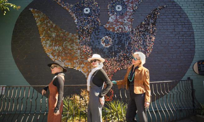 Three women pose in front of street art