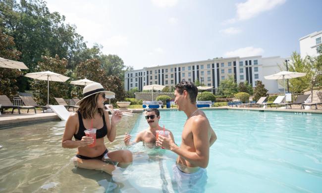 Three guests enjoying drinks in the pool at Guest House at Graceland.